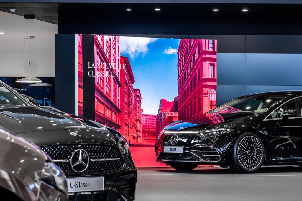 Large format backlit SEG light box display in Mercedes-Benz showroom with vibrant cityscape graphics