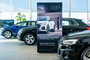 Audi showroom display promoting plug-in hybrid vehicles with a tall branded graphic panel between cars.